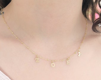 May include: A gold-toned necklace featuring a 16-inch beaded chain with four dangling letter charms spelling the name ZOEY. The text on the image states: MODEL IS WEARING A 16" BEADED CHAIN. SHE IS 5' 2" 120 LBS.