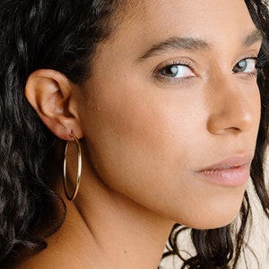 Peut inclure: Une personne portant une paire de grandes boucles d'oreilles en or. Les boucles d'oreilles sont appel&eacute;es "xxlarge leverbacks".