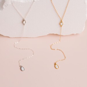 Puede incluir: Dos collares tipo lazo, uno en tono plateado y otro en tono dorado, cada uno con una cadena delicada, un peque&ntilde;o acento de piedra blanca ovalada en el centro y un colgante de piedra blanca ovalada a juego al final de la cadena.