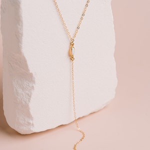 Puede incluir: Un collar tipo lariat dorado con una cadena delicada y dos peque&ntilde;as piedras de &oacute;palo blanco de forma ovalada. Una piedra se sit&uacute;a en la uni&oacute;n central, mientras que la segunda cuelga al final de la cadena vertical, creando una forma de Y.