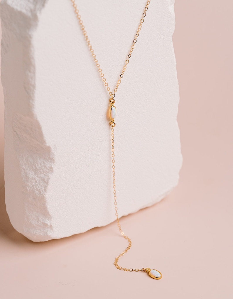Puede incluir: Un collar tipo lariat dorado con una cadena delicada y dos peque&ntilde;as piedras de &oacute;palo blanco de forma ovalada. Una piedra se sit&uacute;a en la uni&oacute;n central, mientras que la segunda cuelga al final de la cadena vertical, creando una forma de Y.
