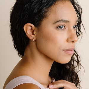 Peut inclure: Une femme portant de petites boucles d'oreilles &agrave; levier dor&eacute;es. Les boucles d'oreilles sont simples et &eacute;l&eacute;gantes, et seraient un excellent ajout &agrave; toute collection de bijoux.