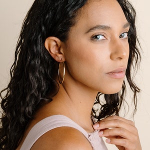 May include: Gold-colored hoop earrings. The earrings are large and circular, with a smooth, polished finish. The model is wearing the earrings. The text in the image says "model is wearing xxlarge leverbacks."