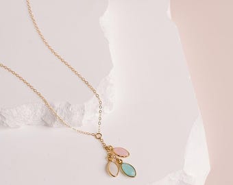 May include: A delicate gold chain necklace featuring three small marquise-shaped charms. The charms include one light pink stone, one light blue stone, and one clear white stone, all suspended together from the center of the thin gold link chain.