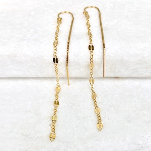 May include: A pair of gold dangle earrings with a delicate chain and small oval links. The earrings are long and thin, and they would be a great addition to any jewelry collection.