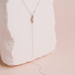 Puede incluir: Un collar tipo lazo de plata con una cadena fina y dos peque&ntilde;as piedras de &oacute;palo blanco de forma ovalada. Una piedra se sit&uacute;a en la uni&oacute;n central en forma de Y y la segunda piedra sirve como colgante al final de la cadena.