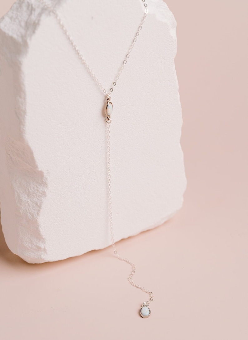 Puede incluir: Un collar tipo lazo de plata con una cadena fina y dos peque&ntilde;as piedras de &oacute;palo blanco de forma ovalada. Una piedra se sit&uacute;a en la uni&oacute;n central en forma de Y y la segunda piedra sirve como colgante al final de la cadena.