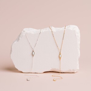 Puede incluir: Dos collares tipo lazo, uno en plata y otro en oro, cada uno con una cadena delicada y un colgante central de piedra blanca en forma ovalada. Los collares se extienden hacia abajo en forma de Y, con un peque&ntilde;o detalle de piedra a juego.