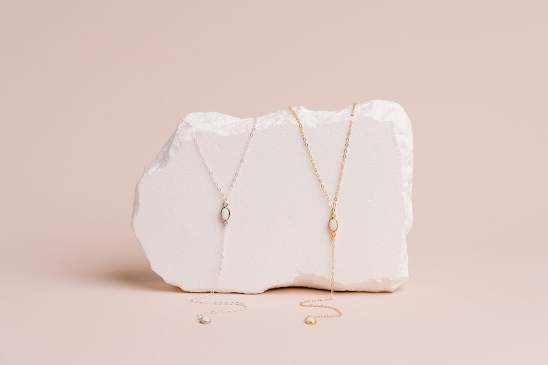 Puede incluir: Dos collares tipo lazo, uno en plata y otro en oro, cada uno con una cadena delicada y un colgante central de piedra blanca en forma ovalada. Los collares se extienden hacia abajo en forma de Y, con un peque&ntilde;o detalle de piedra a juego.