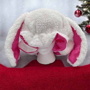 May include: White fuzzy bunny hat with pink satin ears. The hat is on a white mannequin head.