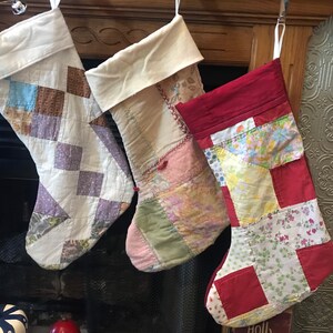 May include: Four patchwork Christmas stockings hanging on a fireplace mantel. The stockings are made of different fabrics and colors, including white, red, pink, and blue. Each stocking has a unique patchwork design.
