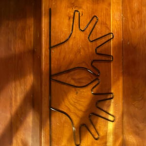 May include: A black metal wall art piece featuring two stylized hand outlines. The hands are connected by a vertical line, creating a symmetrical design. The art is mounted on a wooden surface.
