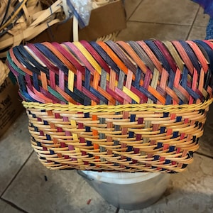 May include: A rectangular woven basket with a vibrant, multi-coloured design. The basket showcases a mix of hues, including red, blue, yellow, and orange, forming an eye-catching pattern. The basket is likely handmade and suitable for storage or decorative purposes.
