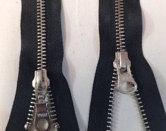 May include: Two black zipper tapes with silver metal teeth and sliders. The zippers are open and the sliders are visible. The left zipper has the brand name "YKK" printed on the slider.