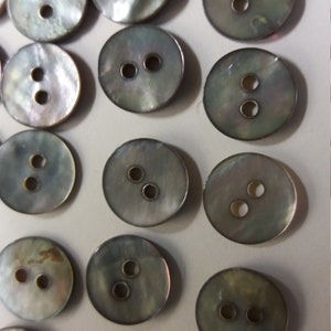 May include: A collection of 18 iridescent, mother-of-pearl buttons with two holes each. The buttons are round and have a slightly textured surface.