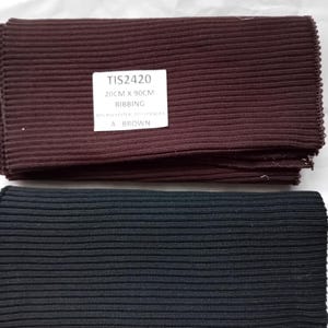 Può includere: Due pezzi di tessuto a costine, uno marrone e uno nero. Il tessuto marrone ha un'etichetta con su scritto "TIS2420 20CM X 90CM RIBBING 80% POLYESTER 20% SPANDEX A BROWN".