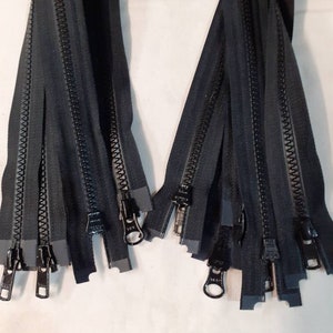 May include: A bundle of black zipper closures with metal pulls. The zippers are arranged in two groups, with the pulls facing outwards.