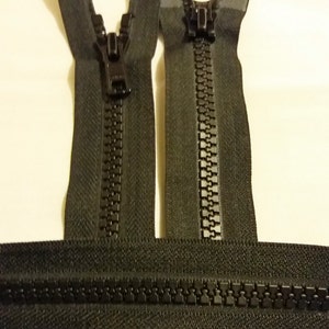 Può includere: Due chiusure a zip nere con denti in metallo e nastro nero. Le cerniere sono disposte a croce.