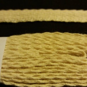 May include: Close-up of a textured, light yellow rope against a black background. The rope appears to be made of woven fibers, with visible ridges and a slightly uneven surface. The image highlights the natural texture and color of the rope.