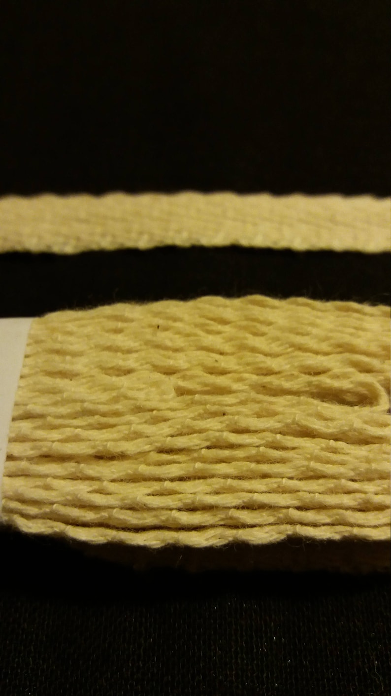 May include: Close-up of a textured, light yellow rope against a black background. The rope appears to be made of woven fibers, with visible ridges and a slightly uneven surface. The image highlights the natural texture and color of the rope.