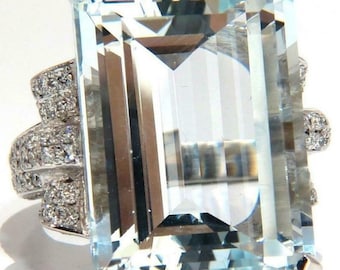 May include: A large, rectangular aquamarine gemstone ring. The light blue gemstone is set in a silver band with smaller, clear gemstones. The ring has a modern, geometric design with a high level of detail and sparkle.