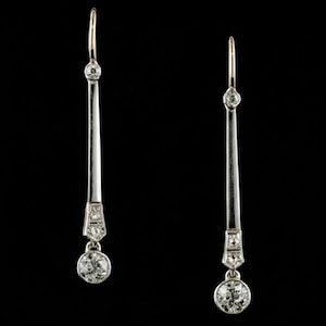 May include: A pair of Art Deco-style drop earrings. Each earring features a gold hook, a small diamond, a silver-toned elongated bar, and a geometric design with small diamonds. A larger, round diamond hangs at the bottom of each earring.