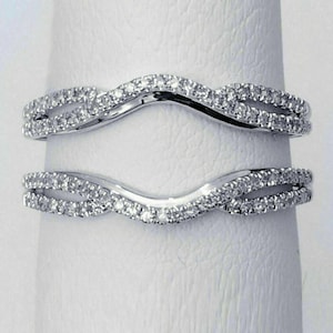 May include: Two curved, silver-toned wedding bands, each encrusted with small, sparkling diamonds. The bands have a wave-like design, with the diamonds set along the top and bottom edges, creating a shimmering effect. The bands are designed to fit together.
