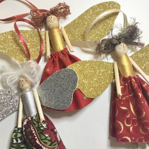 May include: Handmade angel ornaments with wooden peg doll bodies, gold glitter wings, and red fabric skirts. Each angel has a unique hairstyle and ribbon for hanging. Festive holiday decor.