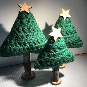 May include: Three handmade Christmas tree decorations. Each tree is crafted from green yarn, with a wooden star on top and a wooden base. The trees vary in size, creating a charming holiday display.