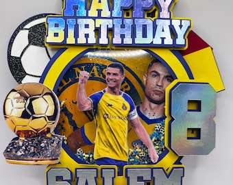 Op de afbeelding: Een gele en blauwe taarttopper met een voetballer, een voetbal, een trofee en de woorden "Happy Birthday Salem".