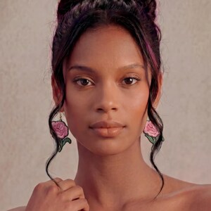 May include: A pair of drop earrings featuring embroidered pink rose blossoms with green leaves. The floral design is detailed with thread stitching, creating a textured appearance. The earrings hang from gold-toned hooks and are labeled STYLE #6.