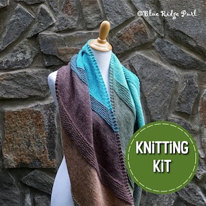May include: A knitting kit featuring a colorful gradient shawl with brown, teal, and green yarn. The shawl is draped over a white mannequin against a stone wall background. The text "Knitting Kit" is written in a circle on a green background.