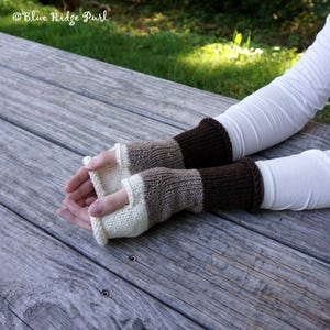 May include: Hand-knitted fingerless gloves in cream, tan, and brown. The gloves have a ribbed cuff and a striped design. The text "Blue Ridge Purl" is in the upper left corner. The gloves are resting on a wooden surface.