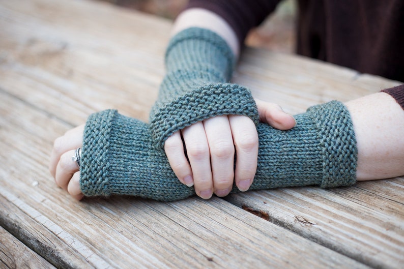 green hand knit wool fingerless gloves with smooth knit center section bordered with textured edges overall length of about 10 inches covers from first knuckle to middle forearm