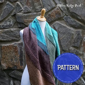 May include: A knitted shawl in shades of brown, teal, and green, draped over a white mannequin against a stone wall background. The text "PATTERN" is displayed in a blue circle.