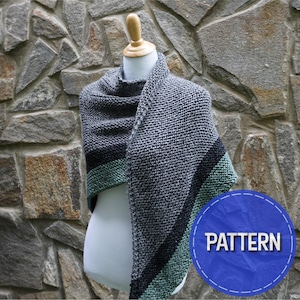 Op de afbeelding: Een grijs en zwarte gebreide sjaal met een groene streep, weergegeven op een mannequin. De sjaal is over de schouders gedrapeerd en toont het getextureerde breipatroon. Een blauwe cirkel met het woord "PATTERN" staat in de rechter benedenhoek.