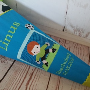 Könnte beinhalten: Ein blauer und grüner Schultüte mit einem Fußball-Design. Die Tüte hat den Namen "Linus" bestickt, sowie einen Fußballspieler und den Text "Einschulung 31.08.2017".