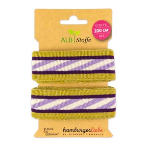 Könnte beinhalten: Zwei Rollen gold- und lila gestreiften Stoffes mit einem Etikett, auf dem "Stripe 200 cm" und "ALB Stoffe" mit einem grünen Blattlogo steht. Das Etikett trägt außerdem die Aufschrift "Made in Germany" und "hamburgerliebe by Susanne Firmenich".