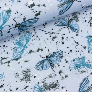 Könnte beinhalten: Hellblauer Stoff mit einem sich wiederholenden Muster aus blauen Schmetterlingen und weißen und schwarzen Farbspritzern.