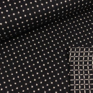 Puede incluir: Tela negra con un patrón de lunares blancos. La tela está doblada sobre sí misma, revelando un segundo lado con un patrón de cuadrícula blanca.
