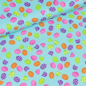 May include: A blue fabric with a repeating pattern of colourful Easter eggs. The eggs are in various shades of pink, purple, orange, and green. Some of the eggs are cracked open, revealing a white interior.