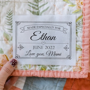 May include: A white fabric label with black text that reads "Made Especially For Ethan June 2022 Love you, Mami". The label is on a pink and white floral fabric.