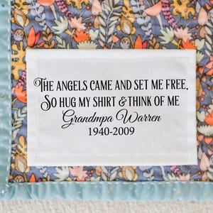May include: A white rectangular patch with black text, stitched onto a floral patterned fabric. The text reads: "THE ANGELS CAME AND SET ME FREE, SO HUG MY SHIRT & THINK OF ME Grandpa Warren 1940-2009". The fabric has a blue, orange, and yellow floral design.