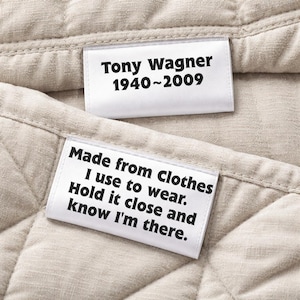 May include: Close-up of two white fabric labels with black text on a beige quilted fabric. One label reads "Tony Wagner 1940~2009." The other label says "Made from Clothes I use to wear. Hold it close and know I'm there."