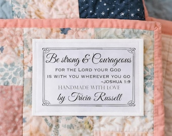 Könnte beinhalten: Eine handgefertigte Steppdecke mit einem Etikett mit der Aufschrift "Sei stark & mutig". Die Steppdecke hat ein Patchwork-Design mit floralen Mustern in Rosa, Blau und Weiß, umrahmt von einem rosa Rand.
