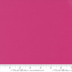 May include: A solid magenta fabric with a ruler along the bottom edge. The fabric has a smooth texture and is evenly colored. The ruler is marked with inch increments. The fabric is likely for sewing or crafting.