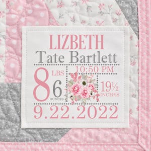 May include: A white fabric square patch featuring pink and grey text and a floral graphic, stitched onto a pink and grey quilted blanket. The text reads: LIZBETH Tate Bartlett, 10:50 PM, 8 LBS 6 OUNCES, 19 1/2 INCHES, and the date 9.22.2022.