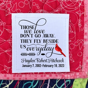 May include: White fabric square with black text that reads "Those we love don't go away. They fly beside us everyday..." with a red cardinal illustration and the name "Hayden Robert Hitchcock" and the dates "January 7, 2002-February 18, 2023".