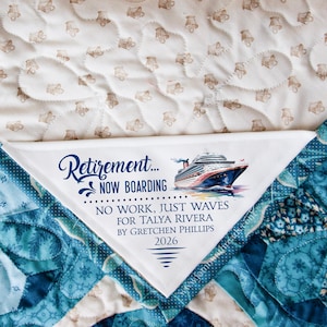 May include: A white and blue quilt with a corner detail featuring the text "Retirement... NOW BOARDING" and a watercolor image of a cruise ship. The quilt has a patterned design and is a retirement gift.