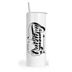 May include: A white cylindrical tumbler with a clear lid and a metal straw. The side features black text that reads I'D RATHER BE QUILTING in a stylized script font, accompanied by a vertical arrow graphic pointing upward next to the word quilting.